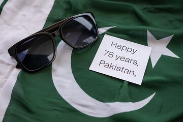 Stylish sunglasses resting on a waving Pakistani flag with a celebratory message for Independence Day