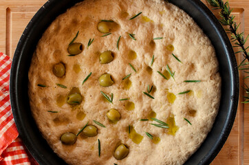 Homemade raw round focaccia with olives, oil and rosemary