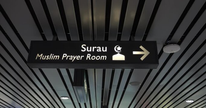 Ceiling sign directs passengers to Muslim Prayer Room in modern international airport. sign, in Malay (Surau) and English, features arrow and distinctive icon.