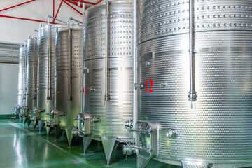 Row of large stainless steel fermentation and storage tanks in modern wine production factory. Industrial wine production in Armenia. Modern winery interior. Food and beverage technology