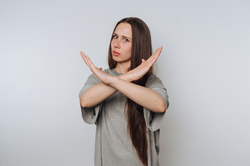 portrait of young woman expresses disapproval by crossing her arms in a negative manner like showing stop sign on light background