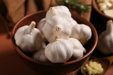 Bowl with fresh garlics on brown background, closeup