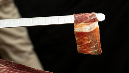 Slice of Iberian ham on carving knife with black background