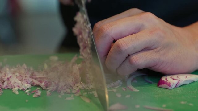 Close up, A chef finely dices a Spanish onion on a green chopping board with a very sharp knife.