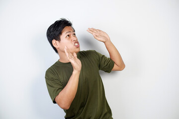 Man appearing surprised or concerned, wearing a green shirt and standing indoors against a plain white background, expressing emotions of fear or worry through his body language and facial expressions