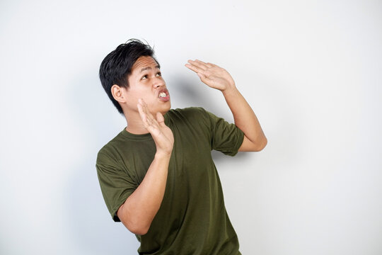 Man appearing surprised or concerned, wearing a green shirt and standing indoors against a plain white background, expressing emotions of fear or worry through his body language and facial expressions
