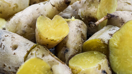 Close-up of cooked yellow sweet potatoes, some sliced to reveal vibrant flesh, showing a heart-shaped piece.