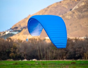 Blue paraglider soaring over a valley