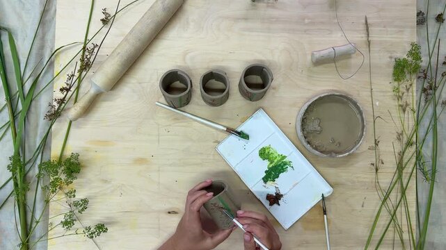 A female artisan applies colorful engobe to handmade clay napkin rings in a video process, adding decorative details and enhancing their natural botanical textures