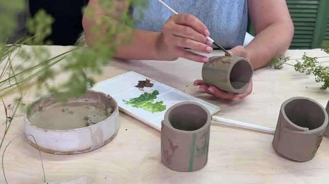 A female artisan applies colorful engobe to handmade clay napkin rings in a video process, adding decorative details and enhancing their natural botanical textures