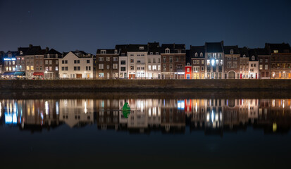 Colorful riverside houses in Maastricht, Netherlands, reflected in still water during the night. Peaceful and atmospheric urban scene.