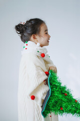 Child in festive attire holding a decorative tree.
