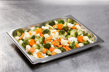 A vibrant assortment of broccoli, cauliflower, and carrots arranged neatly in a stainless steel tray. This healthy vegetable medley is ready for serving in a commercial kitchen setting