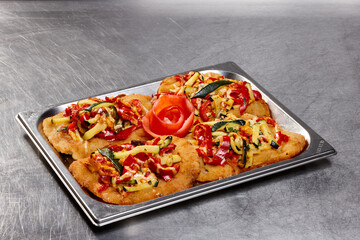 Freshly fried filets are topped with a colorful mix of bell peppers, onions, and zucchini. This appealing dish is artfully presented on a metal tray, showcasing a rose made from tomato