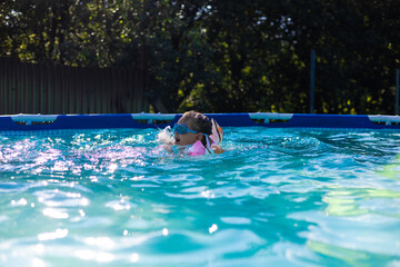 A happy child in goggles and armbands swims in a home pool on a sunny summer day, enjoying the fresh air and learning basic water safety skills. The child swims fearlessly in the pool.