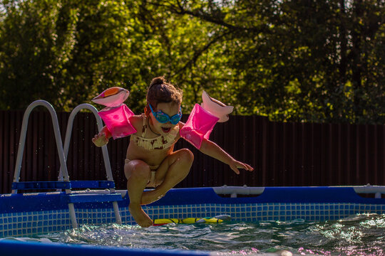 Child swimming in pool. A little girl in glasses and pink armbands jumps into a backyard pool on a sunny summer day, enjoying outdoor games and refreshing water treatments.