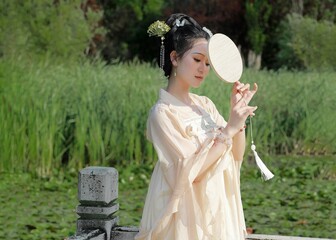 Young Asian woman in traditional attire by a serene pond.