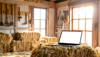 Laptop on hay bales in rustic barn interior with sunlight technology