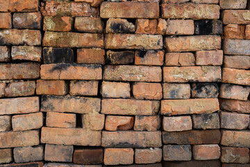 Stacked bricks in various shades of brown and orange create a textured wall, showcasing the unique characteristics of each brick in a rustic and industrial setting with natural lighting