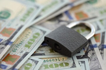 Small black padlock lies on big amount of new hundred US dollar bills