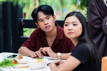 Concerned boyfriend tries to reason with his stubborn and upset girlfriend who refuses to look at him, while having lunch at an alfresco cafe.