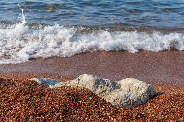 big beautiful white stone lies on coastline and small stones of beach of Adriatic Sea, with beautiful foaming wave, as abstract background of summer travel and vacation