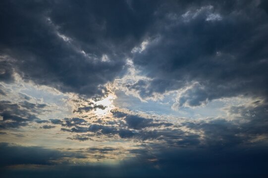 Dramatic cloudy sky with sun rays shining through dark storm clouds over the horizon.