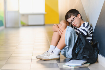 Obraz premium Sad schoolboy crying on floor after bullying from classmates