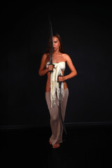 Slender young woman in white cloth holding traditional indian sword low key full length portrait