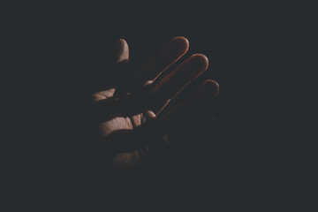 A human hand is illuminated by sunlight in the midst of darkness. The high contrast between light and shadow creates a dramatic and artistic atmosphere. The concept of hope, the search for light, life