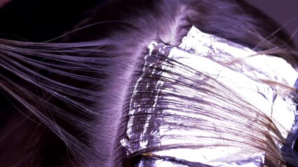 Close-up of a hair coloring process in a salon, where a stylist with red nails applies foil to blonde strands. The scene captures precision, care, and professional technique.
