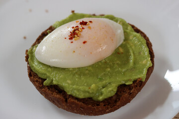 Avocado toast with poached egg and spices on a white plate