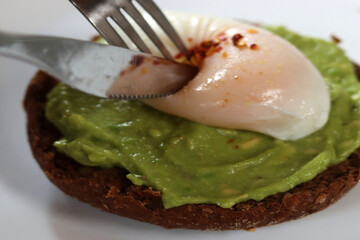 Avocado toast with poached egg and spices on a white plate