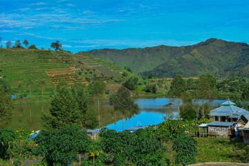 Vibrant natural landscape featuring a calm lake surrounded by lush green, terraced hills and distant mountains. Related to ecotourism, rural development, sustainable agriculture, themes of tranquility