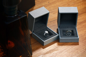 couple of wedding rings in their box on the table with foreground by a liquor bottle of whisky