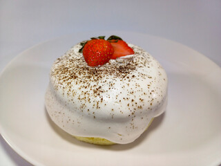 A small, fluffy soufflé pancake covered in a thick layer of white cream and topped with fresh strawberries on a simple white plate. Related to patisserie, desserts, brunch, special culinary art