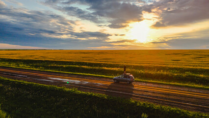 Fototapeta premium a man on the roof of a car in a wheat field at sunset