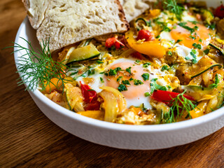 Shakshuka - fried eggs with vegetables and bread on wooden table	