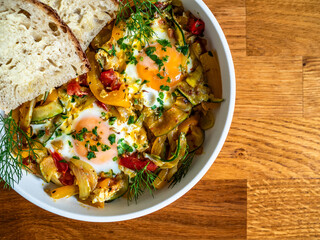 Shakshuka - fried eggs with vegetables and bread on wooden table	