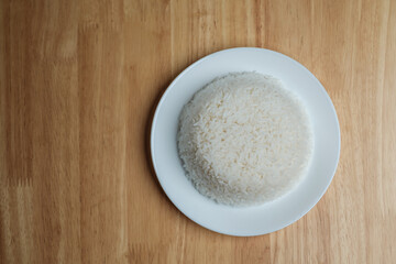 flat lay top view shot of streamed white Thai's jasmine rice in the white clean dish isolated put on the wooden plate dinner table closed to one conner of the photo with empty copy space for texts