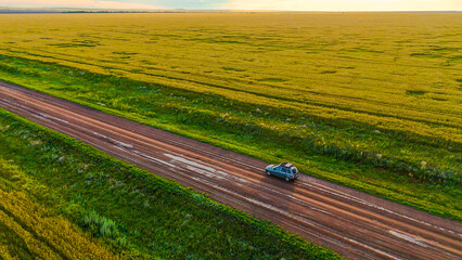 a car on a country road in a wheat field at sunset
