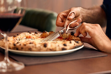 Close-Up of Hands Using Scissors to Cut Pizza on a Restaurant Table