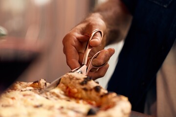 Close-Up of Hand Cutting Pizza with Scissors in Warm Dining Setting