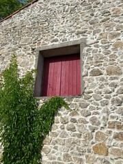 Red wooden shutters and climbing plant on stone wall facade