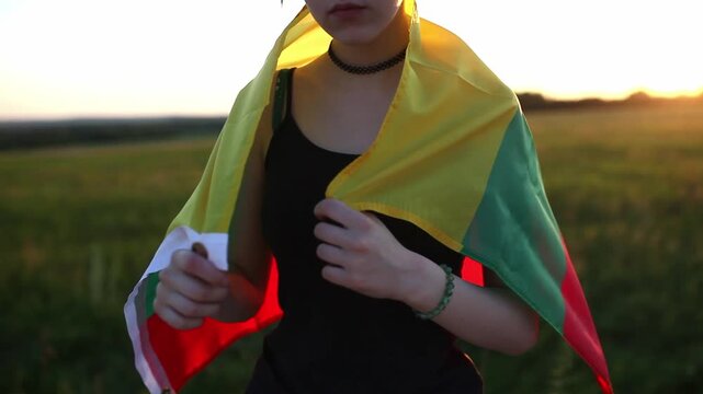 Close up of teen girl covering her shoulders with flag of Lithuania at sunset. Lithuanian Flag Day. Independence restoration Day. Travel and love Lithuania concept. - Powered by Adobe