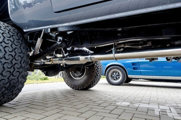 Close-up view of a custom side exhaust pipe and suspension on a lifted off-road vehicle parked on a brick pavement with a parking sign for people with limited mobility. © Igor