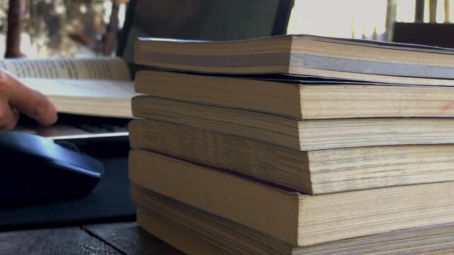 a person reading a book in front of a laptop with several stacks of books.