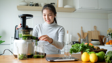 Smiling young woman preparing a healthy green juice using a slow juicer in a bright kitchen.