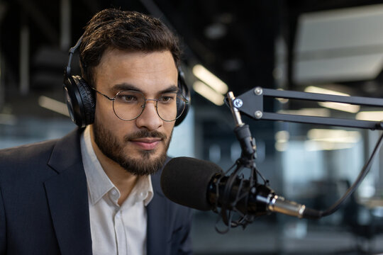 A man wearing headphones speaks into a microphone, likely for a podcast or radio show, with a focused expression.