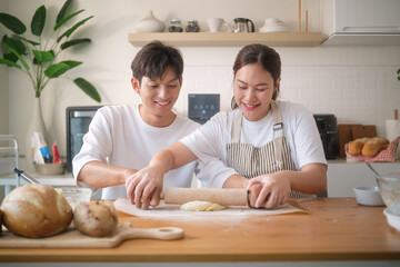 Smiling couple rolling cookie dough together on a wooden table in a modern kitchen.